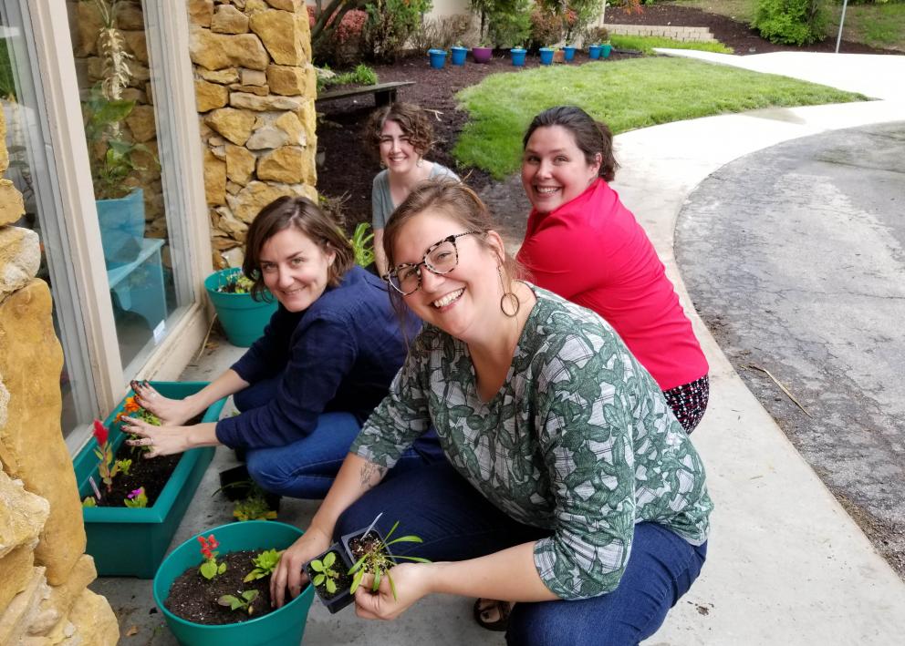 Four female employees plant flowers around the office building.