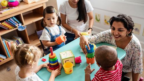 Child care provider sitting at table with 3 children playing with blocks